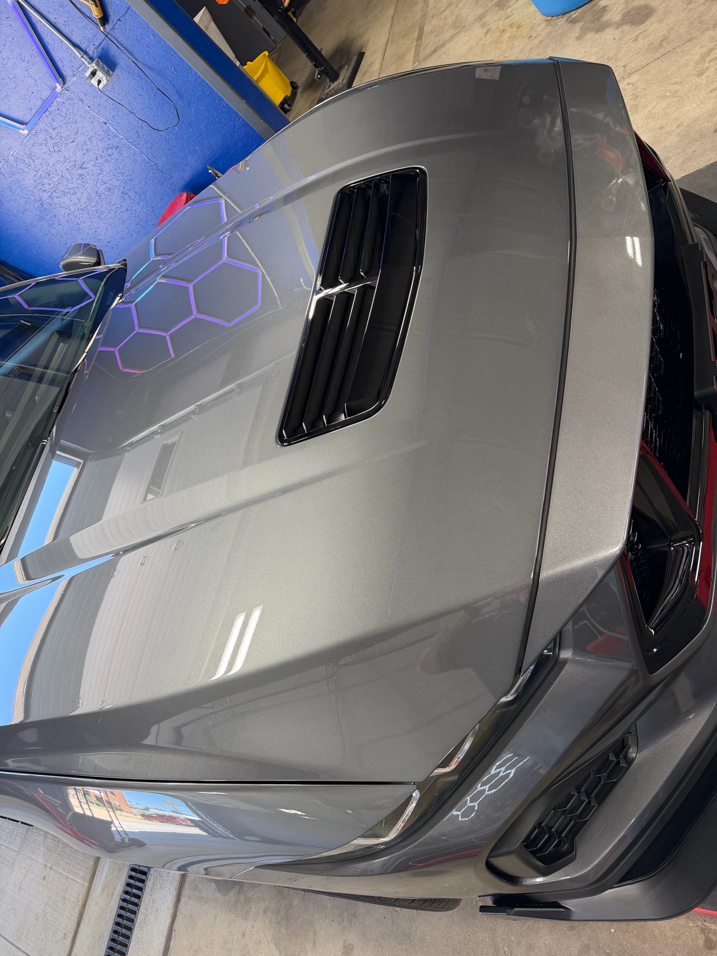 Close view of a gray Mustang hood reflecting the detailing bay lighting
