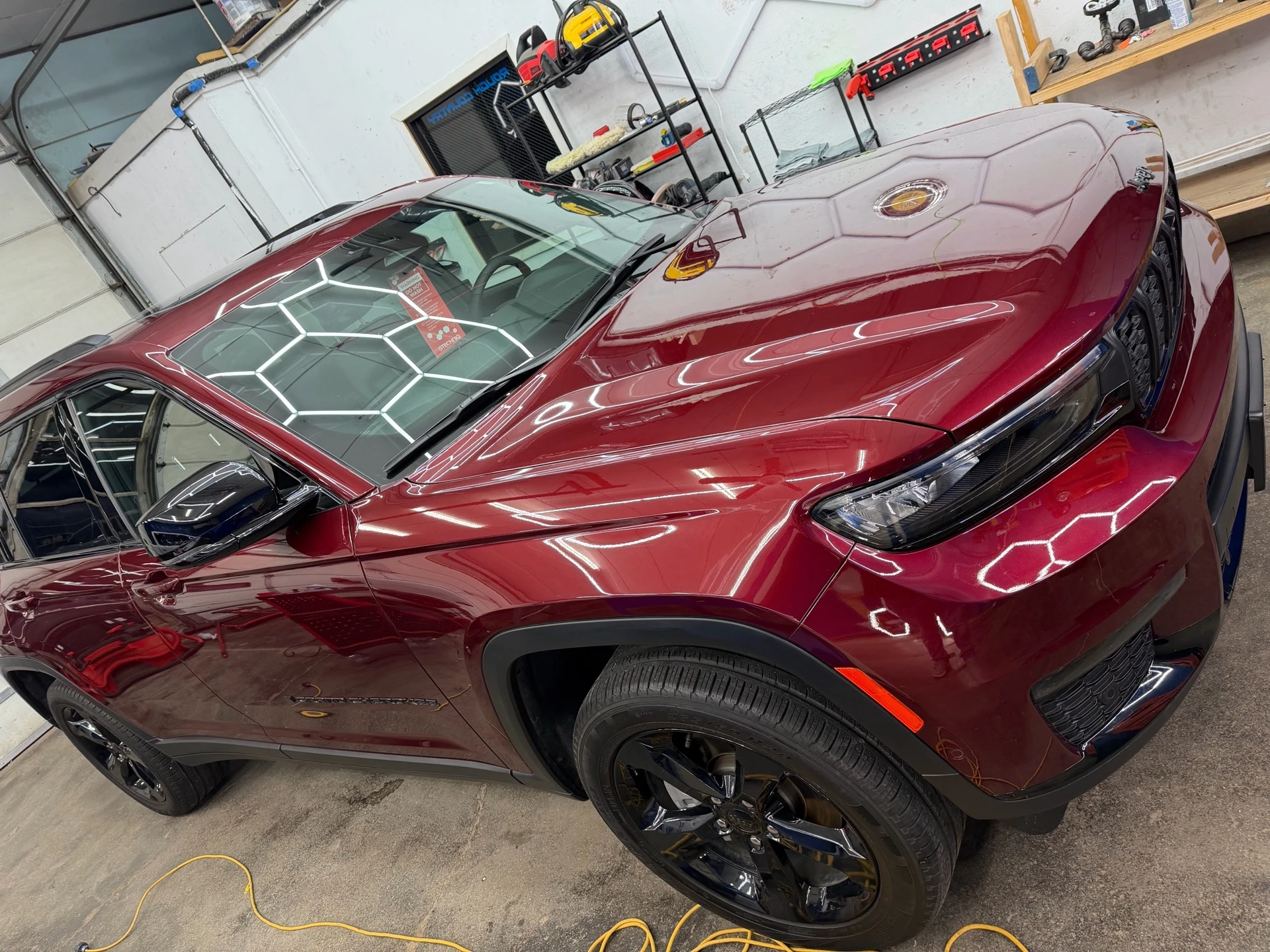 Burgundy Jeep SUV reflecting hexagonal detailing-bay lights across its hood and side panels