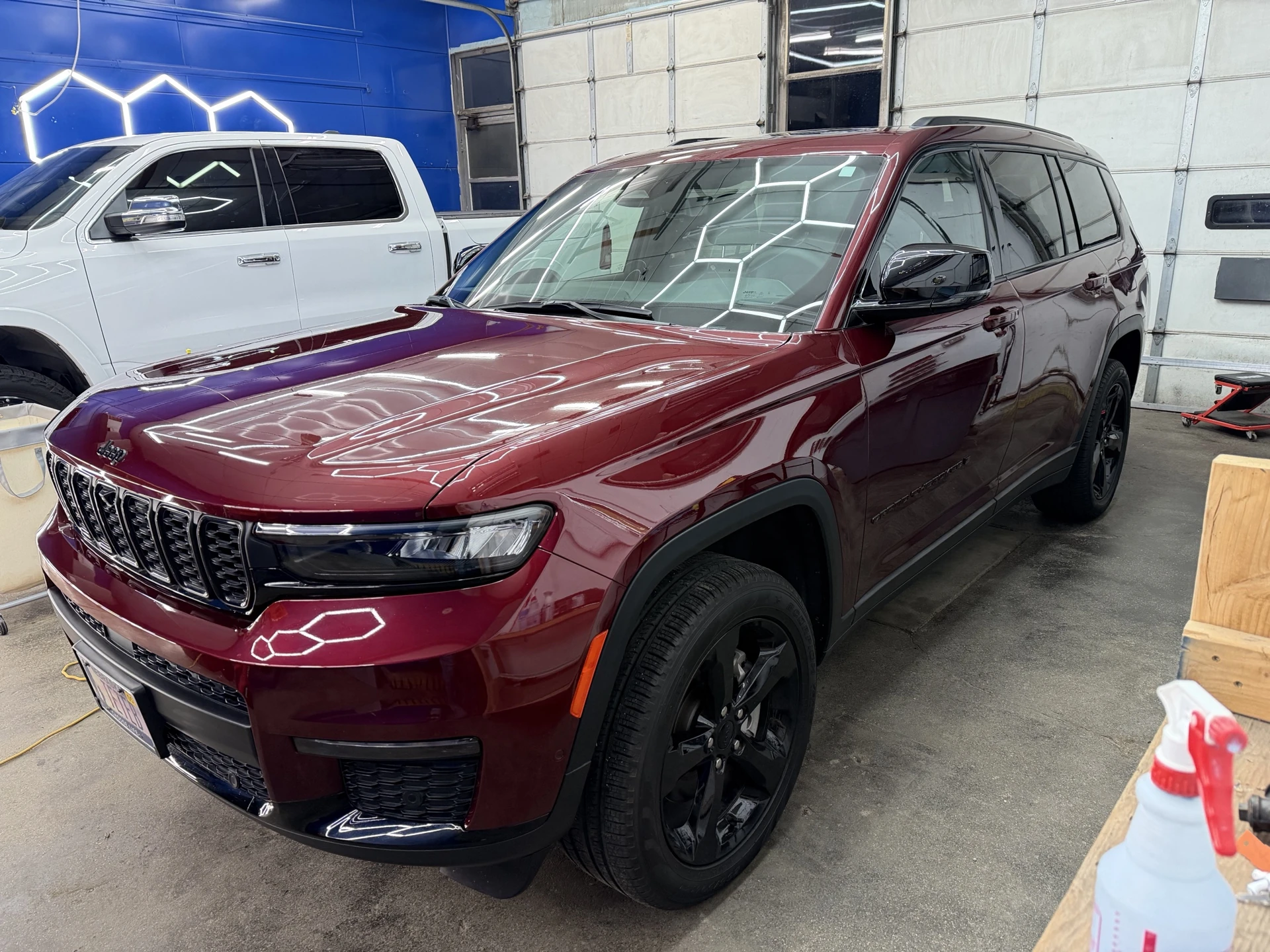 Front three-quarter view of a burgundy Jeep SUV with black wheels inside the detailing bay
