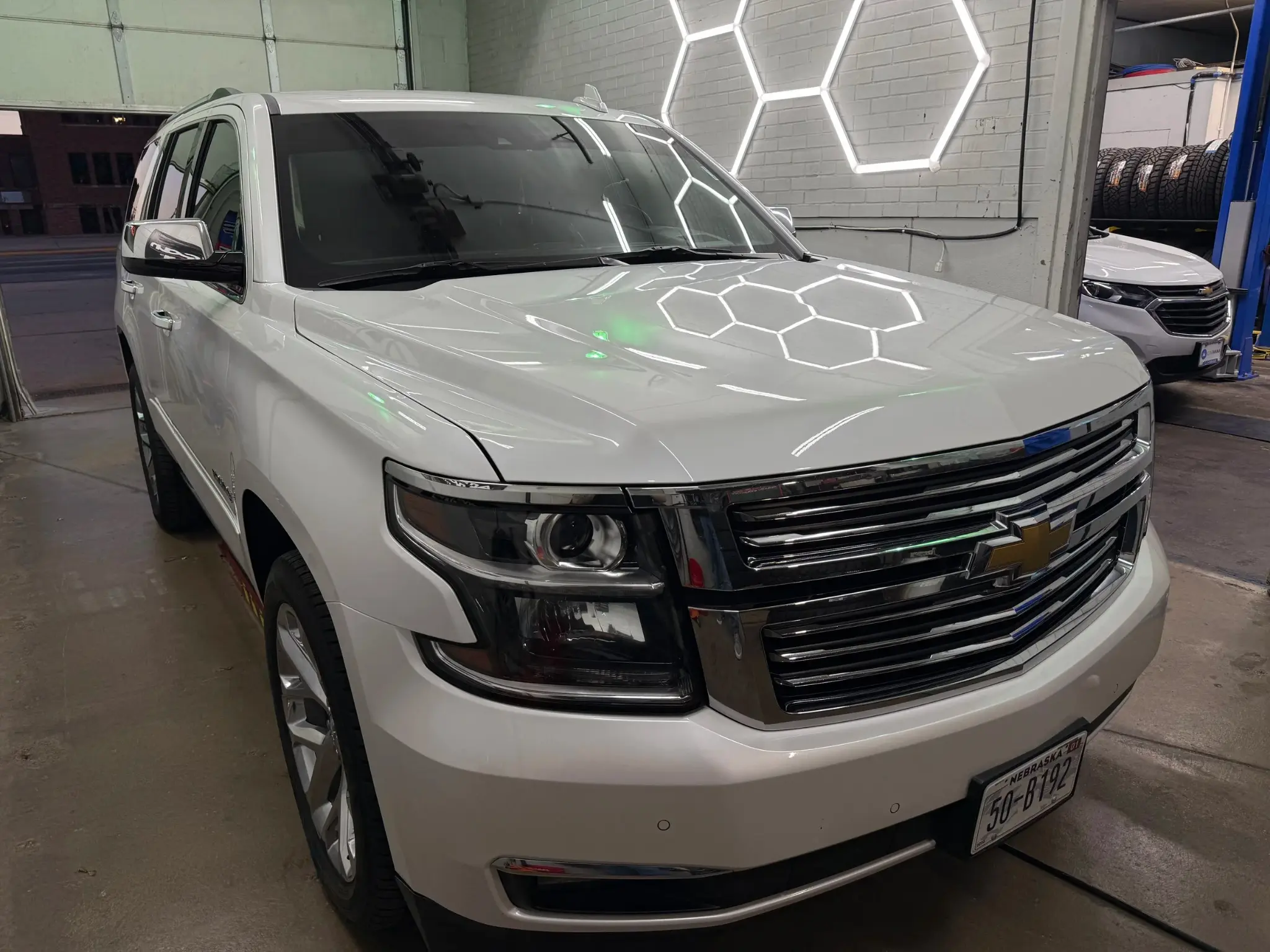 White Chevrolet SUV in the detailing bay reflecting hex lights across the hood